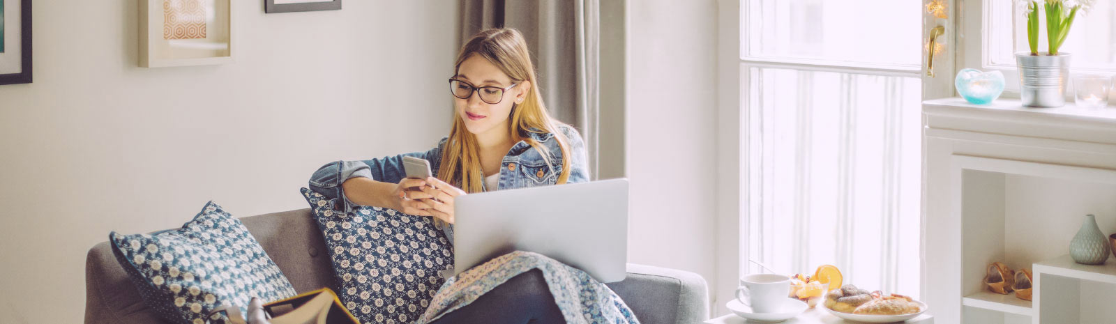 Young woman sitting on couch in the sun looking at her phone.