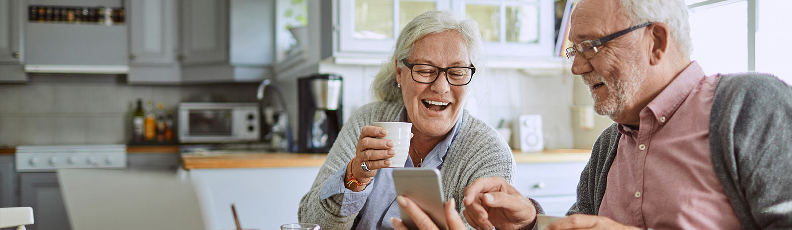 Retired couple having coffee looking at phone.
